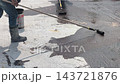 A construction worker applies a bituminous waterproofing layer to an exposed floor surface using a paint roller. This protective coating prevents rainwater leakage into the structure below. 143721876