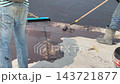 A construction worker applies a bituminous waterproofing layer to an exposed floor surface using a paint roller. This protective coating prevents rainwater leakage into the structure below. 143721877