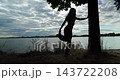 A captivating silhouette of a woman gracefully posed by the tranquil waterside, embodying beauty 143722208