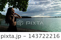 A woman is sitting by the waters edge engaged in a phone call during the beautiful dusk time 143722216
