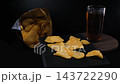 Potato chips rotate on black slate with a drink and open chip package behind them. The scene emphasizes additives and potential health risk. Food safety concept 143722290