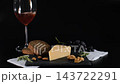Hand pouring wine near composition of fresh cheese with walnuts, almonds, bread and rosemary. Grapes are behind on a black background. Gourmet food and tasting concept 143722291