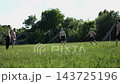 Group of shirtless young men play soccer and passing ball on green field. Amateur footballers training and practice vertical passes outdoor on sunny day. Active guys enjoying friendly football match 143725196