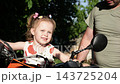 Loving father helps his cute little girl sit on a real adult motorcycle outdoor. Beautiful child holding the handle bars of a big motorbike. Innocent small kid exploring vehicle during family weekend 143725204