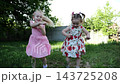 Pretty small girls dancing and playing on green grass lawn outdoor. Two happy sisters spinning in her pink summer dress in sunny garden. Carefree kids enjoying playful childhood moments at nature 143725208