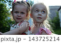 Portrait of two cute little girls in a summer garden. Beautiful happy sisters looking into camera on a bright sunny day. Innocent small children with joyful faces enjoying childhood moments in nature 143725214