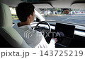 Young businessman relaxes while riding in autonomous self-driving electric car on urban road. Male entrepreneur enjoying comfortable trip on automatic eco vehicle with autopilot system in modern city 143725219