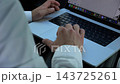 Male hands of entrepreneur typing text on laptop while riding in autonomous self-driving electric car on urban road. Businessman work on notebook during trip in automated eco vehicle with autopilot 143725261