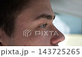 Close up male blue eyes focused on driving automobile on urban road. Face of young driver looking ahead at the road, capturing concentration, deep gaze and calm expression during daytime trip 143725265