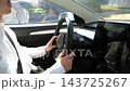 Male hands of young businessman holds steering wheel while driving a modern electric car on urban road. Successful entrepreneur operating an electrical vehicle and commuting to work at sunny day 143725267