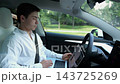 Handsome manager work on his laptop while riding in autonomous self-driving electric car on urban road. Male businessman analyzes data on notebook during trip in automated eco vehicle with autopilot 143725269