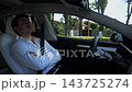 Young businessman relaxes while riding in autonomous self-driving electric car on urban road. Male entrepreneur enjoying comfortable trip on automatic eco vehicle with autopilot system in modern city. 143725274