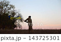 Male military waving blue-yellow banner on liberated territory occupied by russia. Young soldier of ukrainian army lifted flag of Ukraine in honor of victory against russian aggression at dusk 143725301