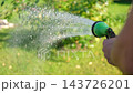 Gardener with a watering hose. Person spraying green grass lawn with hose sprayer. Irrigation with water, sunny day. Garden sprinkler in action. Landscaping. Gardening, waters, growing and plants care 143726201