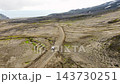 White SUV driving winding dirt road across volcanic plateau with moss patches and distant snowy peaks, aerial landscape view, remote travel scene 143730251