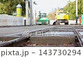 Close view of tram rails and concrete sleepers during track reconstruction in Magdeburg, Germany. Heavy construction vehicle passes camera while municipal workers repair urban transport infrastructure 143730294