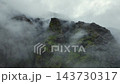 Fog drifting through jagged mossy mountain ridge under overcast sky, aerial wide view, dramatic moody landscape scene, Iceland 143730317