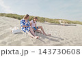 A mother and daughter are sitting on the sand and talking sandy dunes by the sea, 35 years old woman and 15 years old girl wide shot 143730608