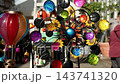 Colorful kinetic wind spinner rotating reflective ornaments decorative hot air balloon displayed outdoor market. Vibrant garden decorations sparkle in sunlight, creating cheerful festive atmosphere 143741320