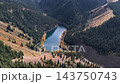 Aerial photography of the golden-hued shores of Lake Kaindy and the coniferous ridges from high above. 143750743
