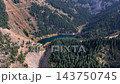 Aerial view over an evergreen ridge, approaching the submerged forest of Lake Kaindy and the autumn-colored lakeshore. 143750745