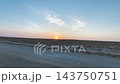 The sun shines low on the wide horizon of Mangystau, with thin clouds and an unpaved road flowing in the foreground. 143750751
