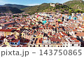 Narrow cobblestone alley in Mediterranean town with tall pastel buildings, shuttered windows and potted plants, warm late-afternoon sunlight and distant hill view 143750865