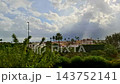 Heavy rain shower in a Mediterranean town with bright sunlight breaking through clouds, creating sparkling illuminated raindrops over green trees and rooftops. 143752141