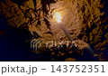 Hand holding a burning candle in a dark underground cave illuminating the rough stone ceiling. 143752351