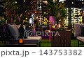 Close up of roses and champagne glasses on rooftop restaurant table with lit city buildings surrounding terrace. Stylish outdoor lounge with wine glasses and lush foliage under ambient night lighting 143753382