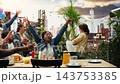 Joyful woman bringing beer bottles to friends at rooftop barbecue party, joining smiling people near grill as they cook patties, socialize and enjoy outdoor gathering with food. 143753385