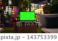 Laptop mockup sits near red roses during romantic rooftop date setup at night. Chroma key notebook beside red flowers beneath colorful terrace lights, close up 143753399