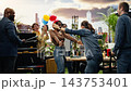 Women sharing warm hug after surprise party reveal with group of friends outdoors, smiling and clapping beside rooftop grill. Celebration and social connection at BBQ cookout. 143753401