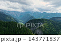 Wide drone shot of deep alpine valley surrounded by steep green forested slopes. Small isolated farmhouses dot valley floor under cloudy sky in Slovenia. 143771837