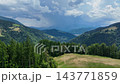 Aerial view of green meadow and dense spruce forest in Savinja region. Dramatic storm clouds hang over distant alpine mountains in Slovenia. 143771859