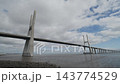 Vasco Da Gama Bridge Rises Over Lisbon Waters, Modern Cable Stayed Bridge With Long Roadway And Tall Pylons. Cloudy Sky Frames Wide River View. 143774529