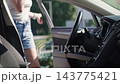 Woman getting into driver seat, starting the engine and fastening seat belt 143775421