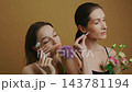 Two women explore beauty techniques with flowers and skincare tools indoors 143781194