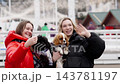 Friends waving happily while holding dogs in a festive outdoor setting 143781197
