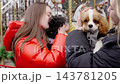 Young woman joyfully hugs small black dog in festive outdoor setting 143781205