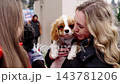 Woman holds a Cavalier King Charles Spaniel at a bustling outdoor event 143781206