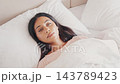 Pensive Young Woman Lying in White Bed. Adult Girl Under Duvet Looking Away And Dreaming While Waking Up. High Angle Shot of Female in Cozy Bedroom Interior With Natural Morning Light. Slow Motion 4k 143789423
