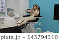 Pedicure specialist tends to womans bare feet as she relaxes in treatment chair and checks smartphone. Gloved practitioner provides foot care in bright salon, with client appearing calm. 143794310
