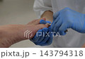 Pedicure practitioner clips toenail while steadying bare foot with blue gloves. Nail care uses metal clippers for careful grooming, with patient relaxed in clean treatment room. Clippers trim nail. 143794318