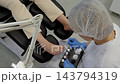 Pedicure treatment focuses on clients toes as technician carefully applies nail polish. Gloved nail care professional selects products from nearby bottles while client sits in salon chair. 143794319
