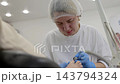 Pedicurist carefully files clients toenail with electric nail drill in bright salon. Gloved technician focuses on foot care, guiding rotating tool during detailed pedicure treatment. 143794324