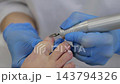Pedicure treatment uses electric nail file on clients toenail as technician steadies foot with gloved hands. Nail care professional focuses on careful shaping during salon service. 143794326