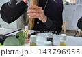 Woman making custom perfume during a creative workshop. She mixes essential oils with a dropper and funnel to create a unique fragrance.  143796955
