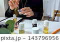 Woman making custom perfume during a creative workshop. She mixes essential oils with a dropper and funnel to create a unique fragrance.  143796956