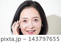 A middle-aged Japanese woman smiles while checking the wrinkles around her eyes; an image of anti-aging care and skincare for women in their 50s. 143797655